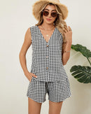 Model wearing gingham sleeveless V-neck top and matching shorts set, carrying woven handbag, casual summer style